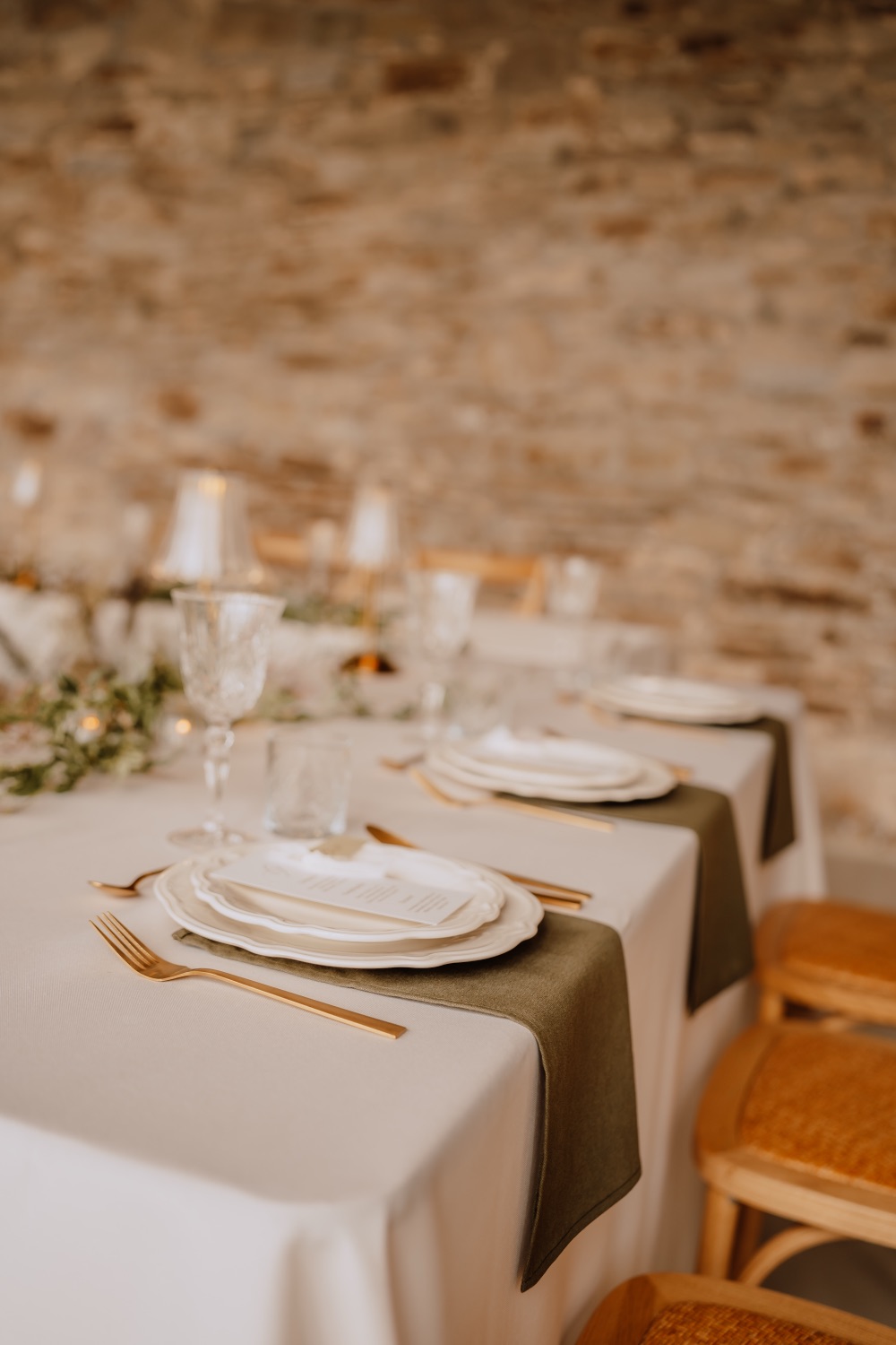 Eingedeckte Gedecke mit Gläsern, goldenem Besteck und Kerzenlicht vor Natursteinwand
